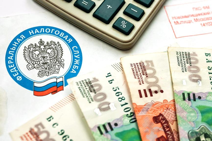 Эмблема Федеральной налоговой службы России, калькулятор, денежные купюры и платёжные документы на столе — иллюстрация к новости об отмене штрафов и пеней